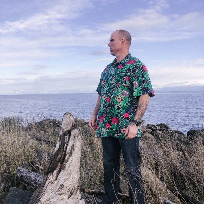 man in hawaiian shirt on rocks by ocean